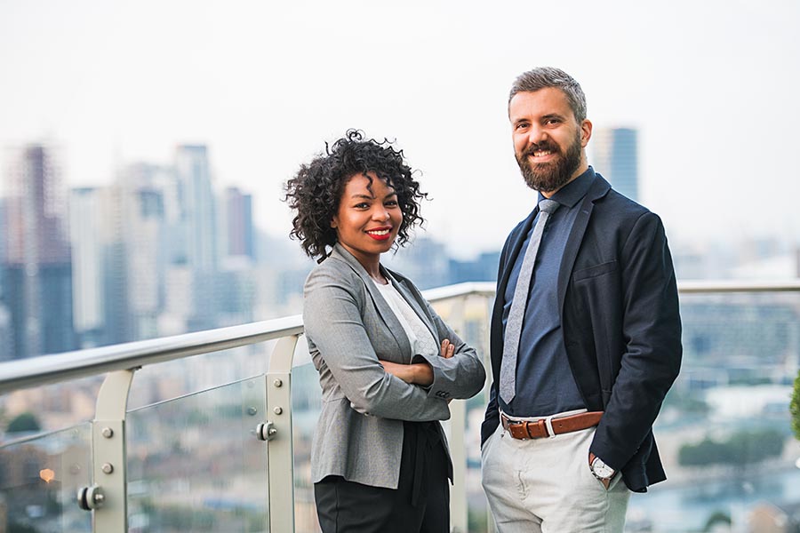 Employee Benefits - Two Smiling Coworkers Stand on a Balcony on a High Rise Office Building
